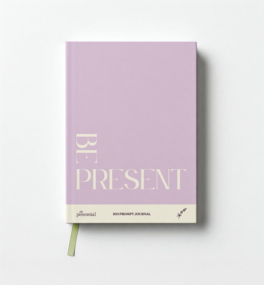 A lavender-colored guided journal with the title 'BE PRESENT' on the cover, along with the brand 'in Perennial' underneath. It includes a ribbon marker on the side.